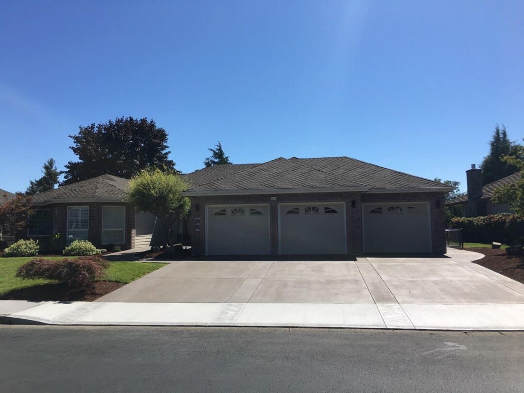 A suburban home with a triple garage and a wide, well-maintained concrete driveway under a clear blue sky.