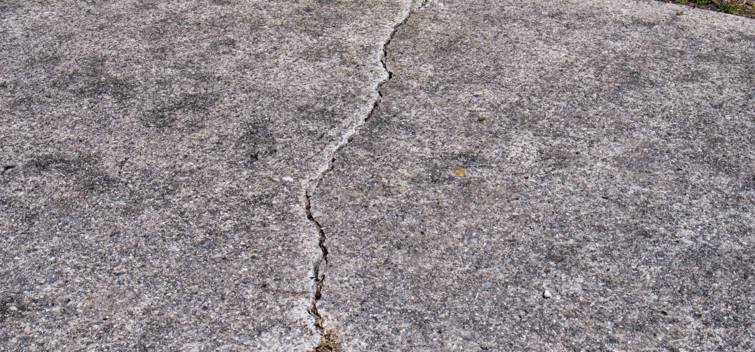 Cracked concrete slab with a long uneven fracture running across the surface, creating a potential trip hazard.