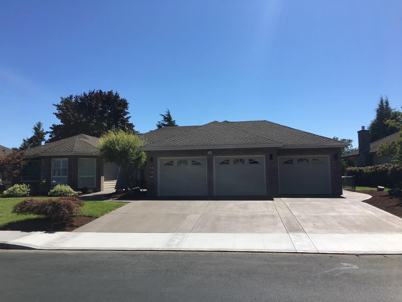A suburban home with a triple garage and a wide, well-maintained concrete driveway under a clear blue sky.
