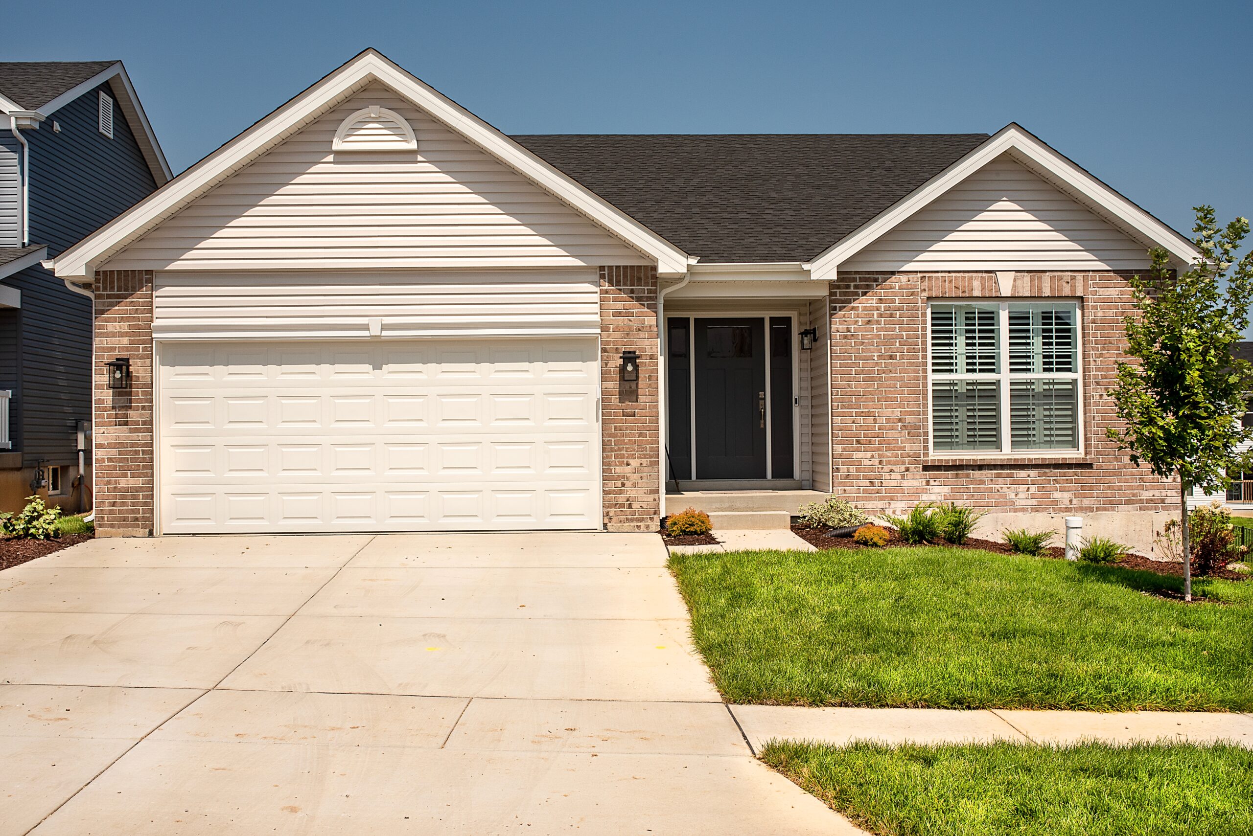 A single-story suburban house with a brick and siding exterior, a two-car garage, a concrete driveway, and a small landscaped yard.
